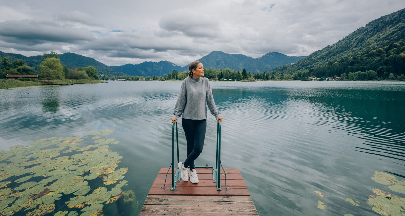 Reha Patientin steht am Privat-Steg am Tegernsee mit Bergkulisse im Hintergrund